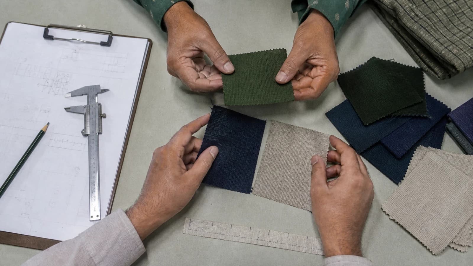 Hands comparing woven fabric swatches beside measuring tools